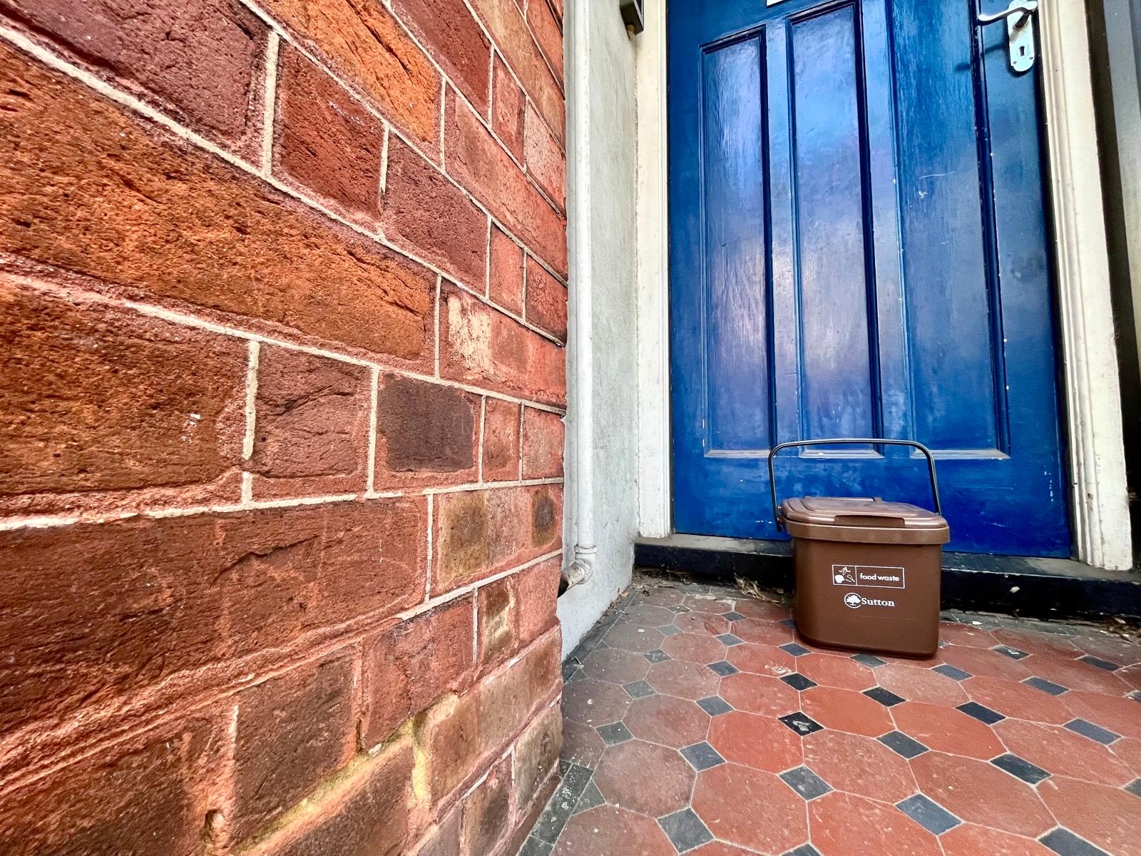 A brown food waste caddy in front of a blue door