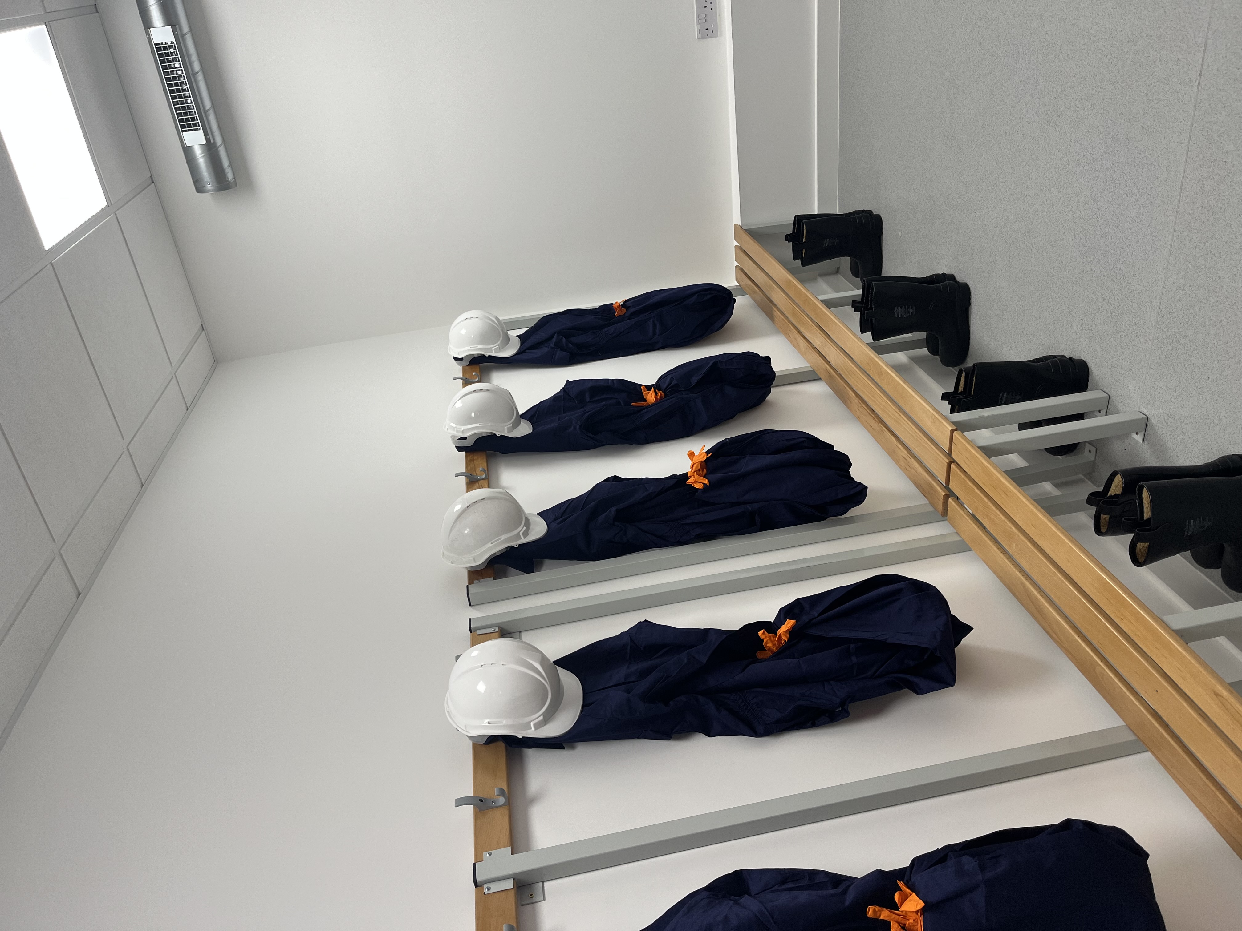 Image shows construction boots, hats and overalls hanging up