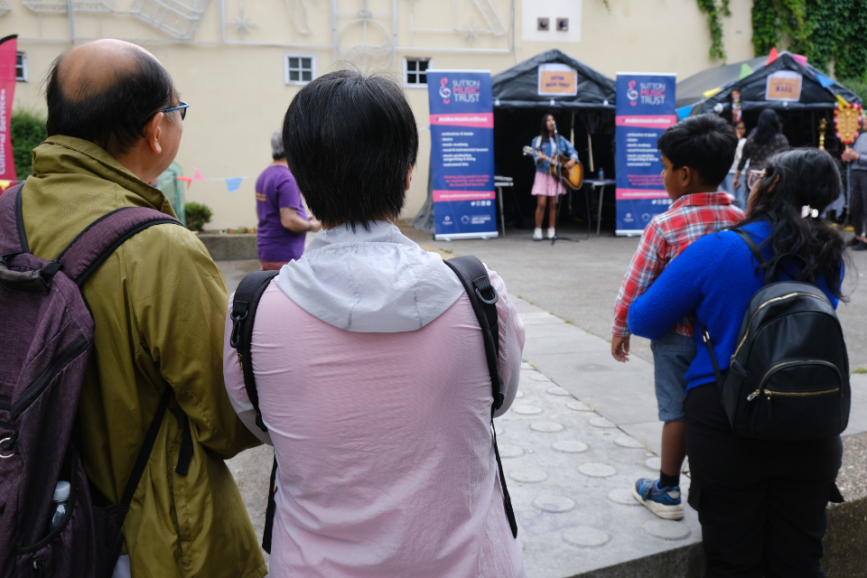 Small crowd of people watching a young woman playing the guitar and singing