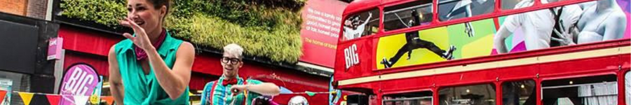 Two dancers on a high street in front of a red bus