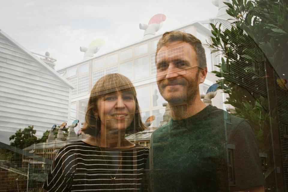 A man and woman's faces superimposed over a picture of trees and a building