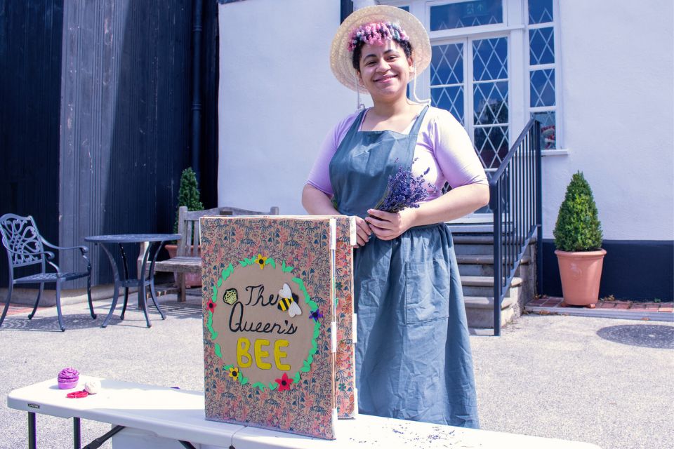 Actress Shaunna Duffy stood smiling behind a large book saying the following on the front cover: The Queen's Bee