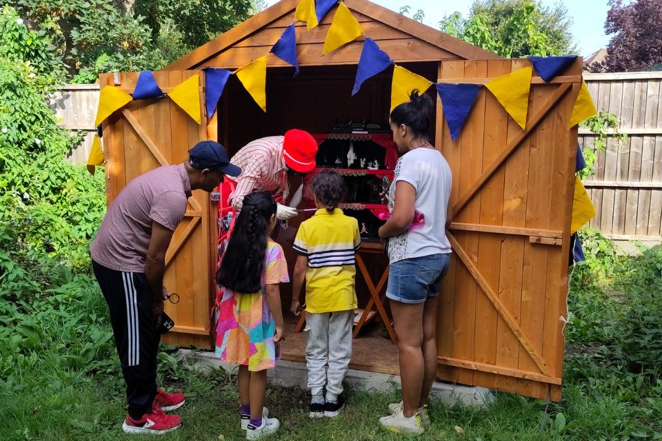 Three adults and two children looking into a shed containing a small cabinet filled with surreal trinkets and models