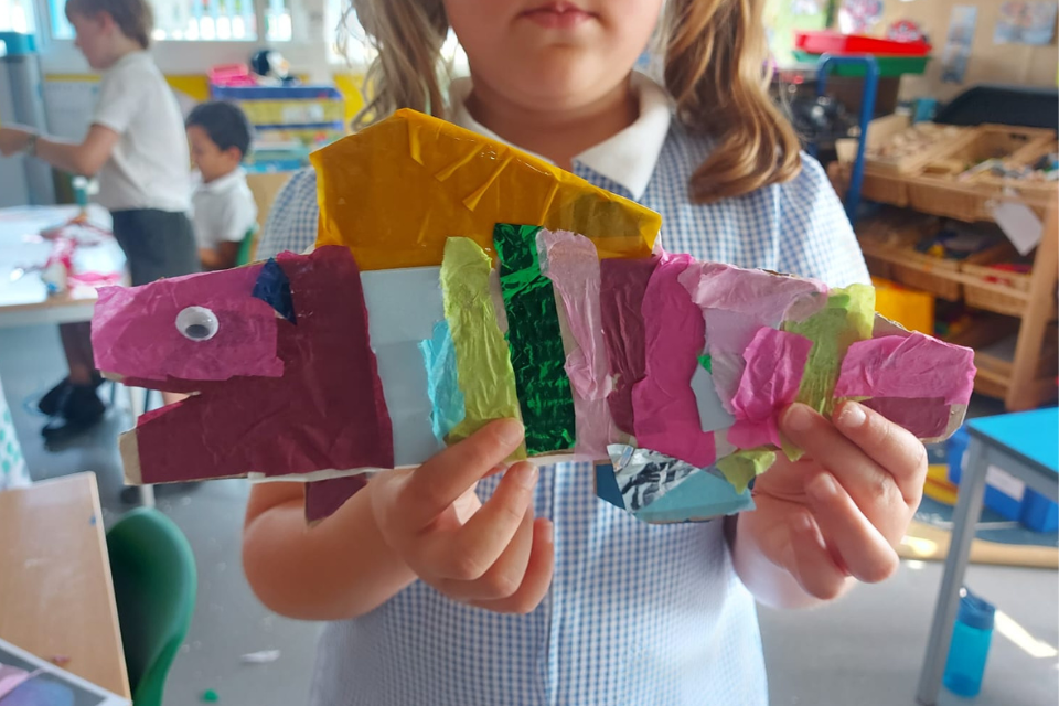 A small child holding a colourful craftwork fish