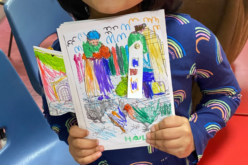 A young girls pair of hands holding a small book visibly coloured in by the child