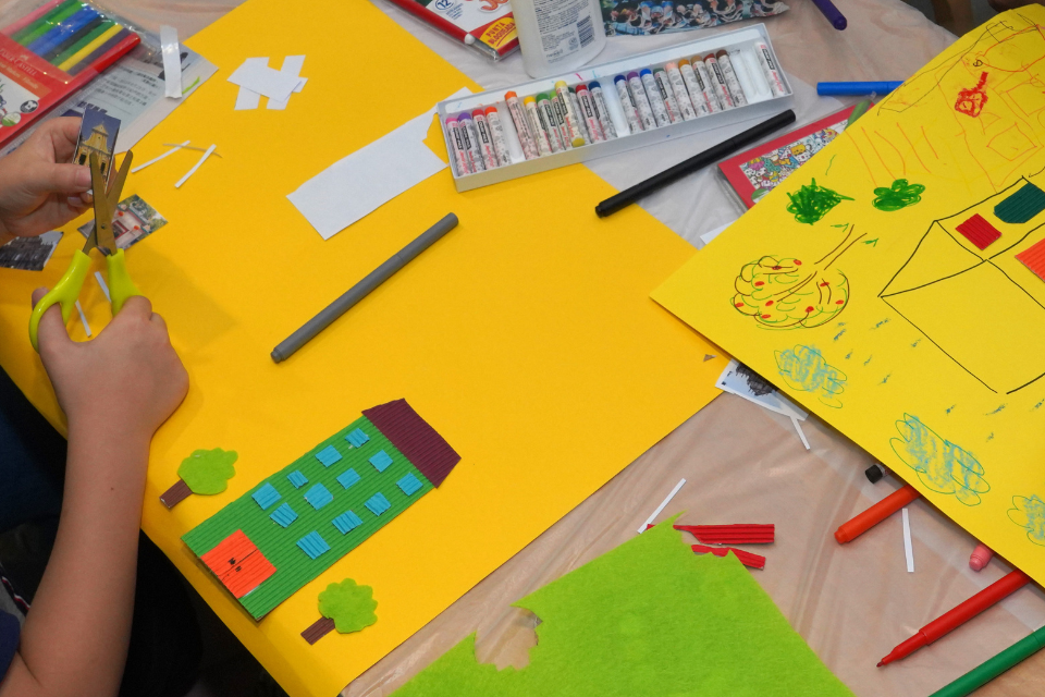 Several pieces of coloured paper and felt tips as a child's hands assemble their craft picture