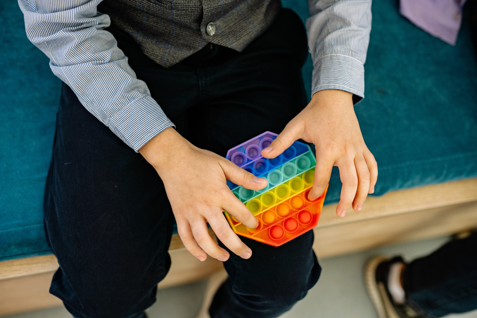 A pair of hands playing with a colourful toy that contains plastic finger holes