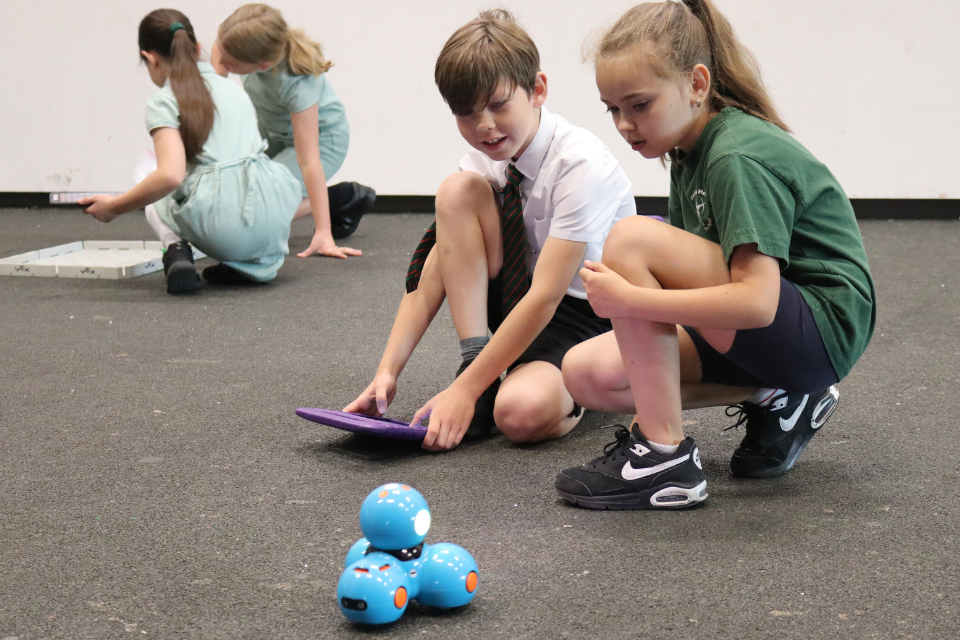 Two Robin Hood pupils using an iPad to control a small robot made of four blue spheres