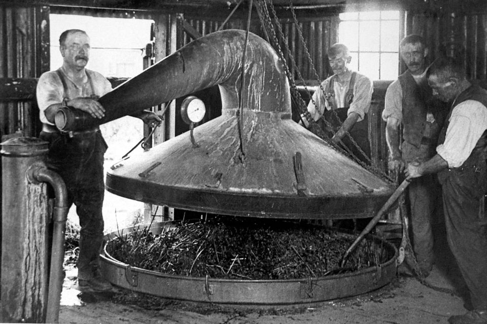 black and white photo of four men operating a distillation machine