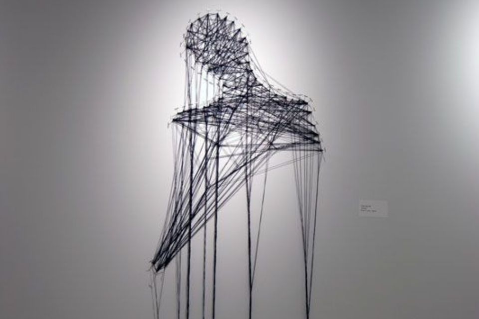 An artpiece consisting of several black wires attached together in a crosshatch fashion forming the shape of a human head, neck and shoulders
