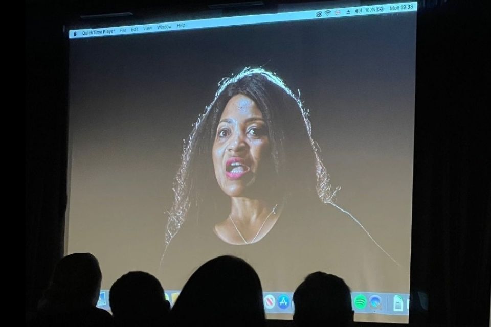 A cinema screen showing a woman's face with an open mouth exclamation towards the viewer