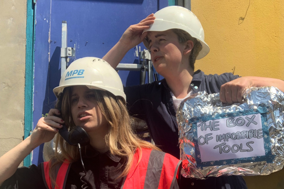 Two women wearing safety helmets with one of them holding a toolbox wrapped in aluminium foil