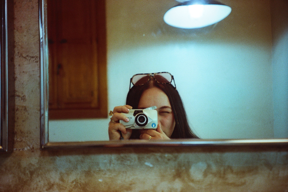 A picture of the reflection of young woman looking through the disposable camera in the mirror