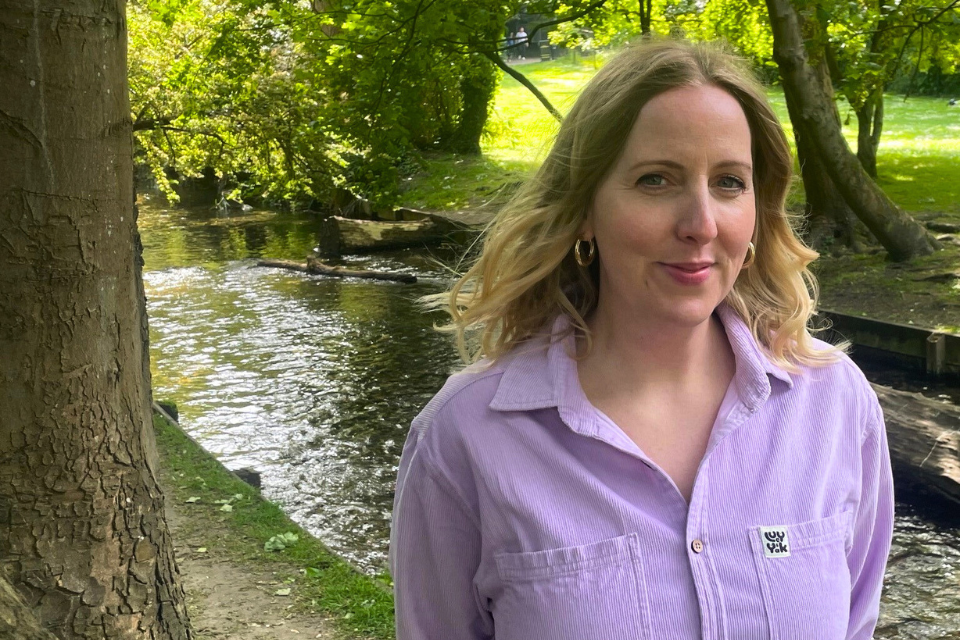 A smiling young blonde woman stood next to a river